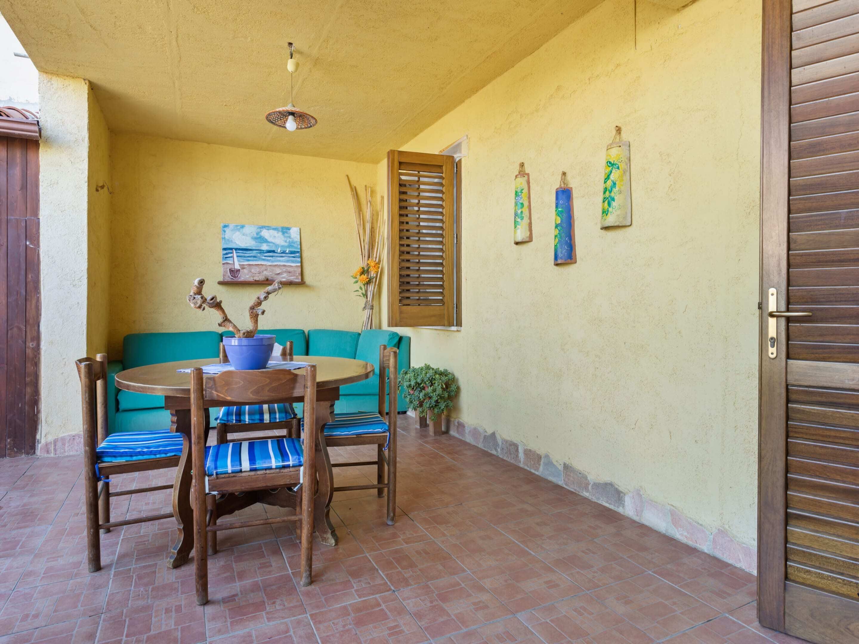 A patio with a round wooden table, two chairs, a turquoise sofa, and a wooden door.