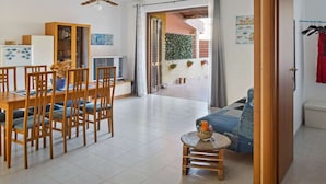 A spacious living area with a dining table, chairs, a sofa, and a small round table with a bowl and a bottle. There is a television and a cabinet with glass doors. - Cosy Holiday Home in Sanremo With Sea Beach Nearby (Alcamo)