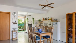 A modern kitchen with wooden cabinets, a dining area with a table and chairs, and a view of a garden through an open door. - Cosy Holiday Home in Sanremo With Sea Beach Nearby (Alcamo)