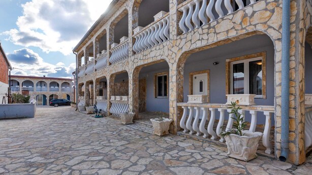 A courtyard with stone flooring, a building with multiple balconies, and a car parked nearby.