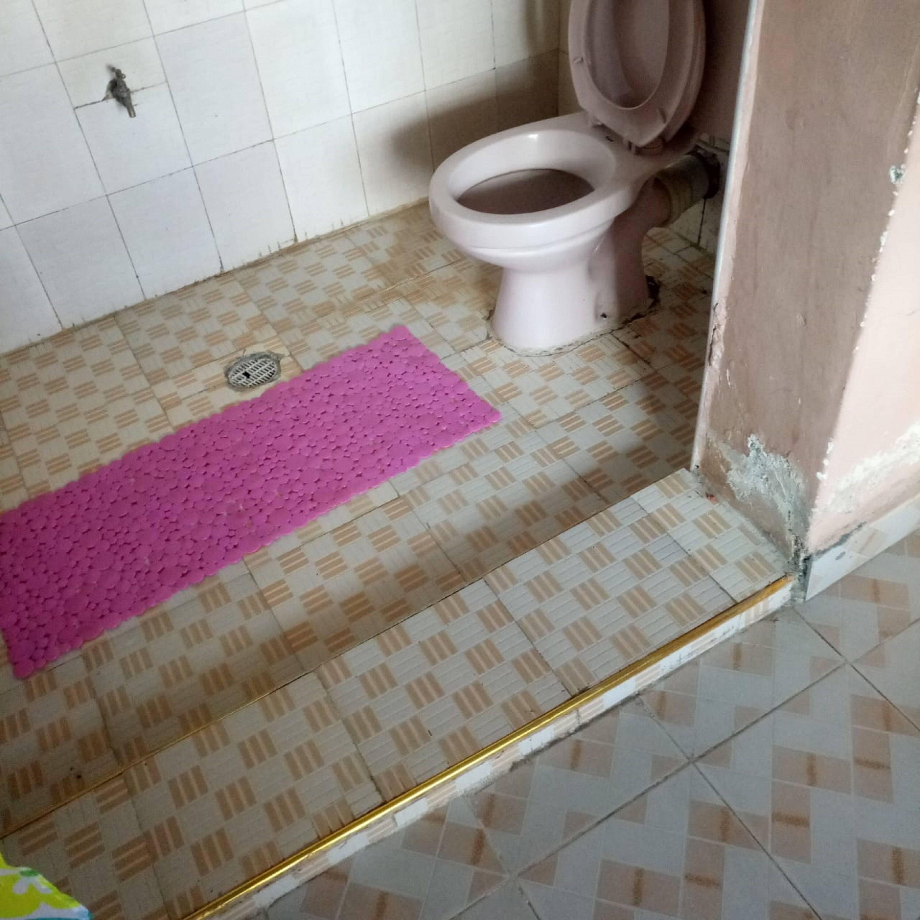 Une salle de bain avec un carrelage à motifs, un tapis rose, des toilettes et un drain.