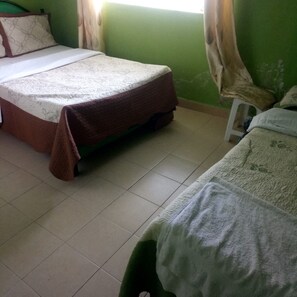 Una habitación con dos camas, una pared verde y una ventana con cortinas.