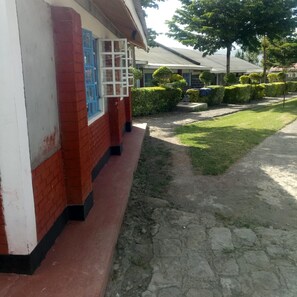 Un edificio con paredes de ladrillo rojo y fachada blanca, un sendero rojo y negro que conduce a una zona ajardinada con arbustos bien cuidados y un árbol.