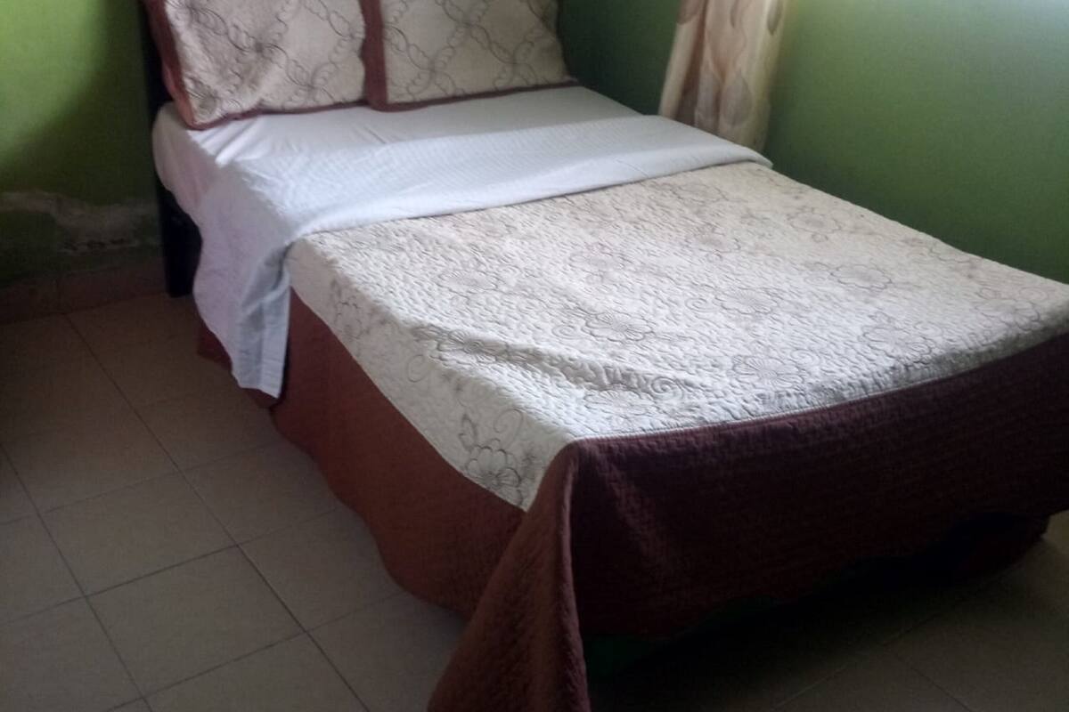 A small, single-bed room with a green headboard, white bedding, and a brown throw blanket.