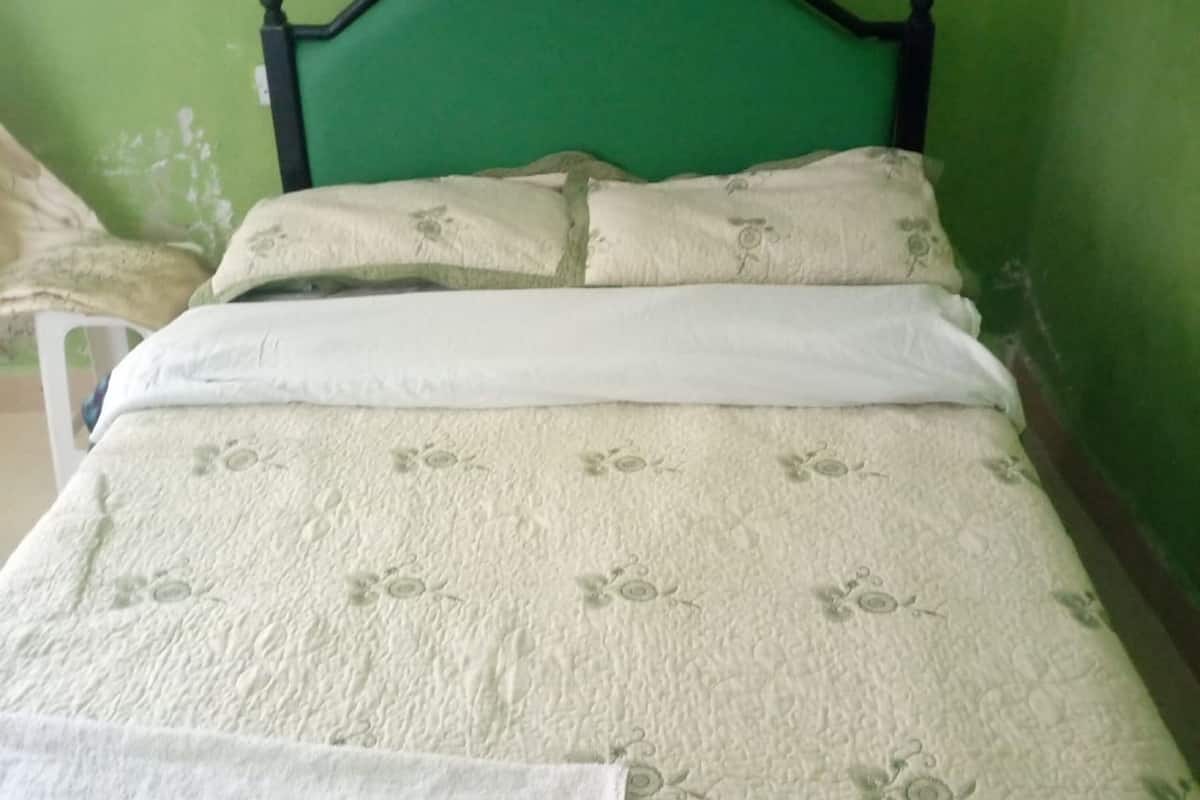 A bed with a floral-patterned bedspread and matching pillows, a white blanket, and a green headboard.