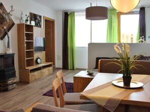 A modern living room with a wooden entertainment unit, a dining table with chairs, and a potted plant. - Boutique Apartment in Lungau With Terrace (Weisspriach)