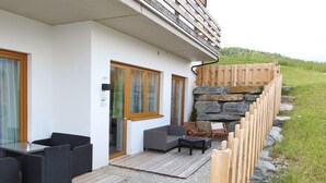 En moderne udendørs terrasse med fletmøbler, en stenvæg og en træterrasse.
