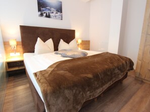 A neatly made bed with a brown blanket, white pillows, and a headboard. There are two bedside lamps on either side of the bed. - Boutique Apartment in Lungau With Terrace (Weisspriach)