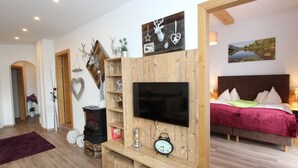 En moderne stue med et træ-tv-bord, et fladskærms-tv og en seng med et rødt sengetæppe i baggrunden.