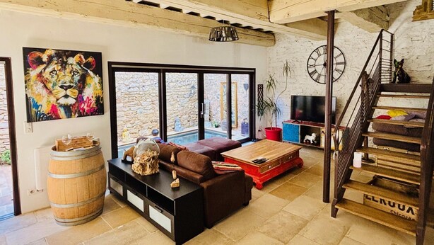Un amplio espacio de sala con una pared de piedra, un ventanal grande, un barril de madera, un sofá de cuero marrón, un reposapiés rojo, un televisor y una escalera.