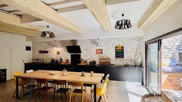 A modern kitchen with a stone wall, wooden beams, a dining table with colorful chairs, and a large window.