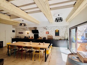 A modern kitchen with a stone wall, wooden beams, a dining table with colorful chairs, and a large window. - Olonzac Escape: Pool & Charm (Olonzac)