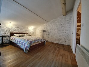 A bedroom with a wooden floor, a bed with patterned bedding, a white wardrobe, and a textured wall. - Olonzac Escape: Pool & Charm (Olonzac)