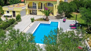 Una villa amarilla con piscina, mobiliario exterior y vistas a las montañas.