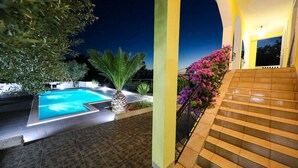 Una piscina con solárium empedrado, una escalera con barandilla y un parterre con flores rosas.