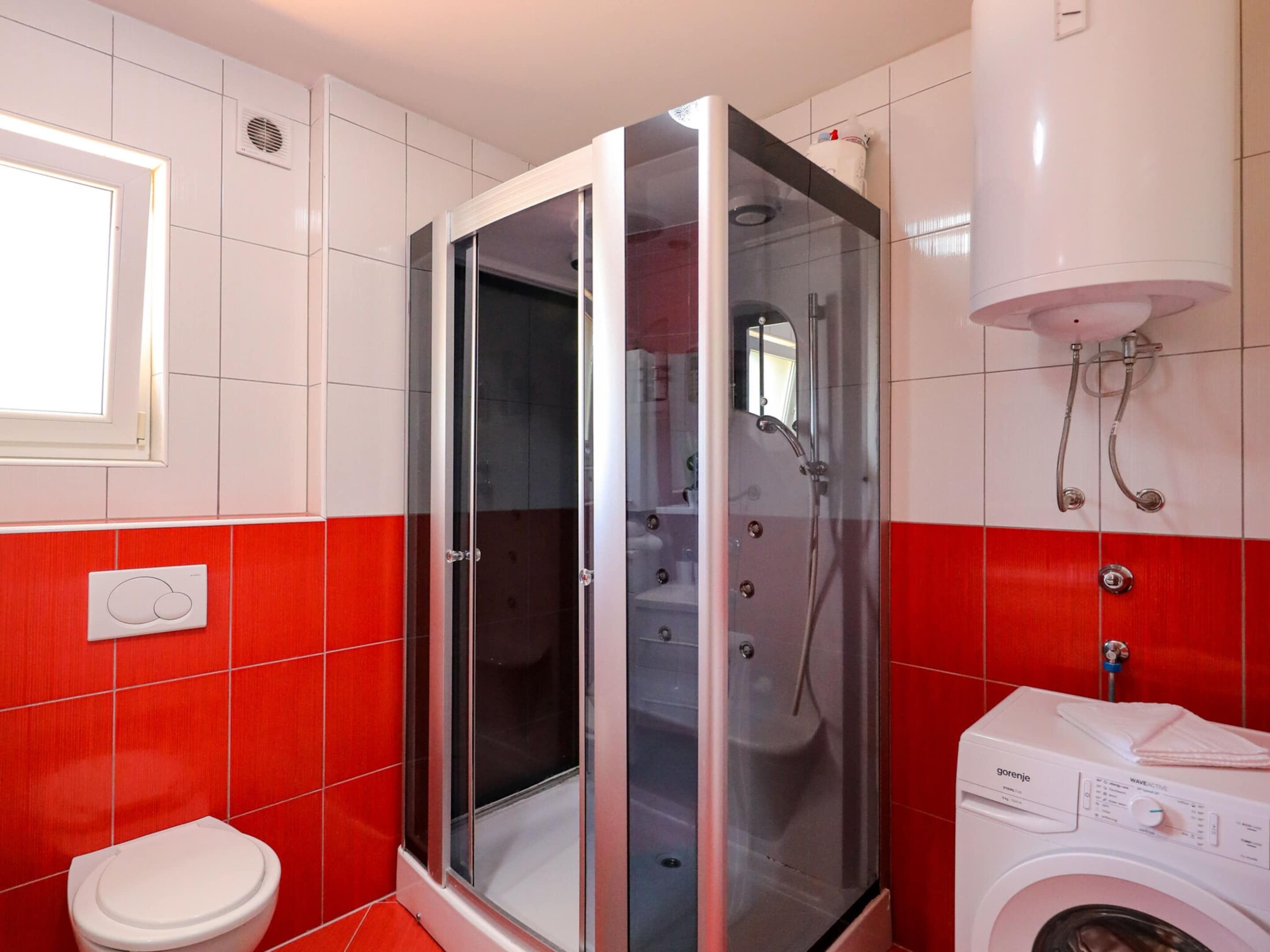 Un bagno con cabina doccia in vetro, un water bianco e una lavatrice.