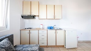 A compact kitchen with white cabinets, a small refrigerator, and a window providing natural light. - Tasteful Apartment in Zadar With Balcony (Zadar)