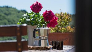Ein rustikaler Tisch im Freien mit einer Metall-Kaffeekanne, zwei schwarzen Tassen und einem Korbwäscher.