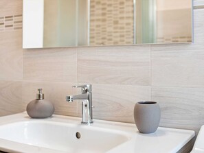 A bathroom with a white sink, a modern faucet, and a gray vase on the counter.