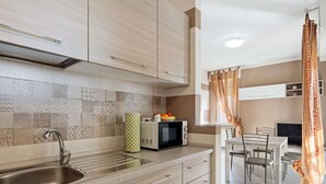 A modern kitchen with a stainless steel sink, a microwave, and a fruit bowl on the counter. There is a dining area with a table and chairs visible. - Belvilla by OYO APT 7 Villa DEI Pini (Ameglia)
