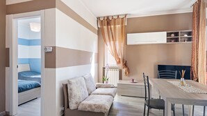 A modern, compact living space with a sofa, a dining table, and a small kitchen area. - Belvilla by OYO APT 7 Villa DEI Pini (Ameglia)