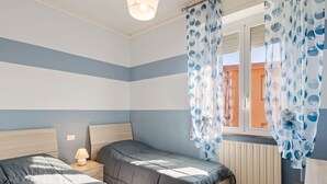 A bedroom with two beds, a window with curtains, a bedside lamp, and a radiator. - Belvilla by OYO APT 7 Villa DEI Pini (Ameglia)