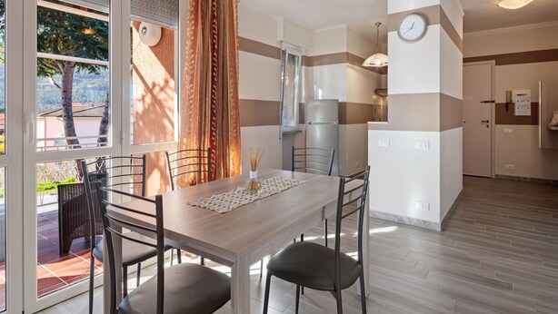 A modern kitchen with a refrigerator, a clock, and a dining area with a table and chairs. - Belvilla by OYO APT 7 Villa DEI Pini (Ameglia)