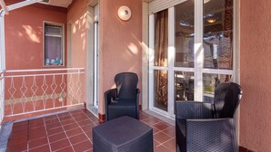 A covered patio with two wicker chairs and a small table, a window with curtains, and a door. - Belvilla by OYO APT 7 Villa DEI Pini (Ameglia)