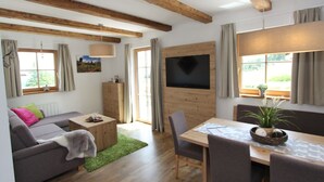 A cozy living room with a sofa, a wooden dining table, and a TV mounted on the wall. - Cozy Chalet in Weisspriach With Terrace (Weisspriach)