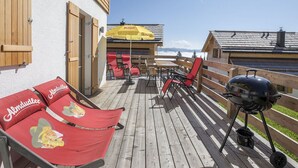 A wooden deck with lounge chairs and a barbecue grill, overlooking a mountainous landscape. - Cozy Chalet in Weisspriach With Terrace (Weisspriach)