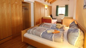A cozy bedroom with a wooden bed, a wardrobe, and a window with curtains. - Spacious Apartment in Langenfeld With Sauna (Laengenfeld)