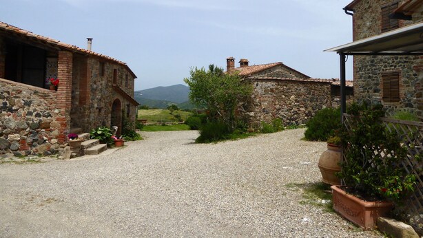 A stone building with a gravel driveway and a view of distant mountains. - Belvilla by OYO Livorno (Castelnuovo di Val di Cecina)