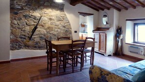 A dining area with a stone wall, wooden ceiling beams, and a tiled floor. - Belvilla by OYO Livorno (Castelnuovo di Val di Cecina)