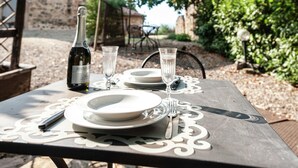 A table set outdoors with a bottle of wine, two glasses, plates, and cutlery. - Belvilla by OYO Livorno (Castelnuovo di Val di Cecina)