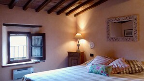 A bedroom with a bed, a window, a bedside table with a lamp, a mirror, and a radiator. - Belvilla by OYO Livorno (Castelnuovo di Val di Cecina)
