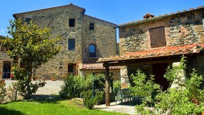 A stone building with a tiled roof, a covered patio with chairs, and a small garden area. - Belvilla by OYO Livorno (Castelnuovo di Val di Cecina)