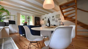 A dining area with a round table, white chairs, a hanging light fixture, and wooden beams on the ceiling.