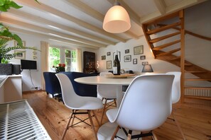 Un coin repas avec une table ronde, des chaises blanches, un luminaire suspendu et des poutres en bois au plafond.