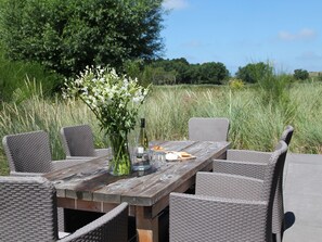 An outdoor dining area with wicker chairs and a wooden table, surrounded by tall grass and trees. - Dune Villa in Egmond aan Zee (Egmond aan den Hoef)