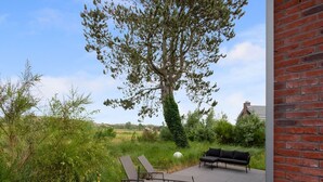 Une terrasse extérieure avec deux chaises longues et une table, entourée de verdure et d’un mur de briques.
