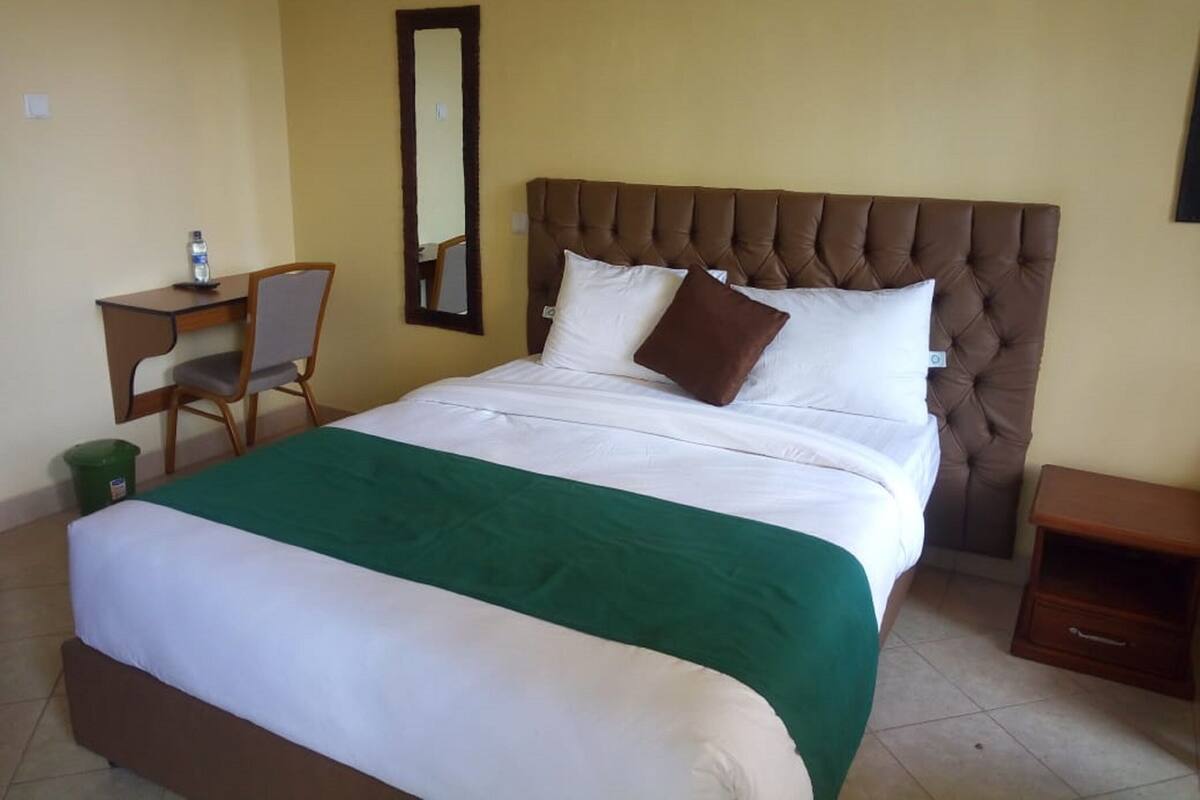 A hotel room with a bed, a desk, a chair, a mirror, and a nightstand.