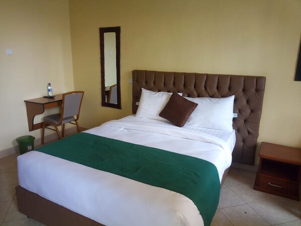 Habitación de hotel con cama, escritorio, silla, espejo y mesita de noche.