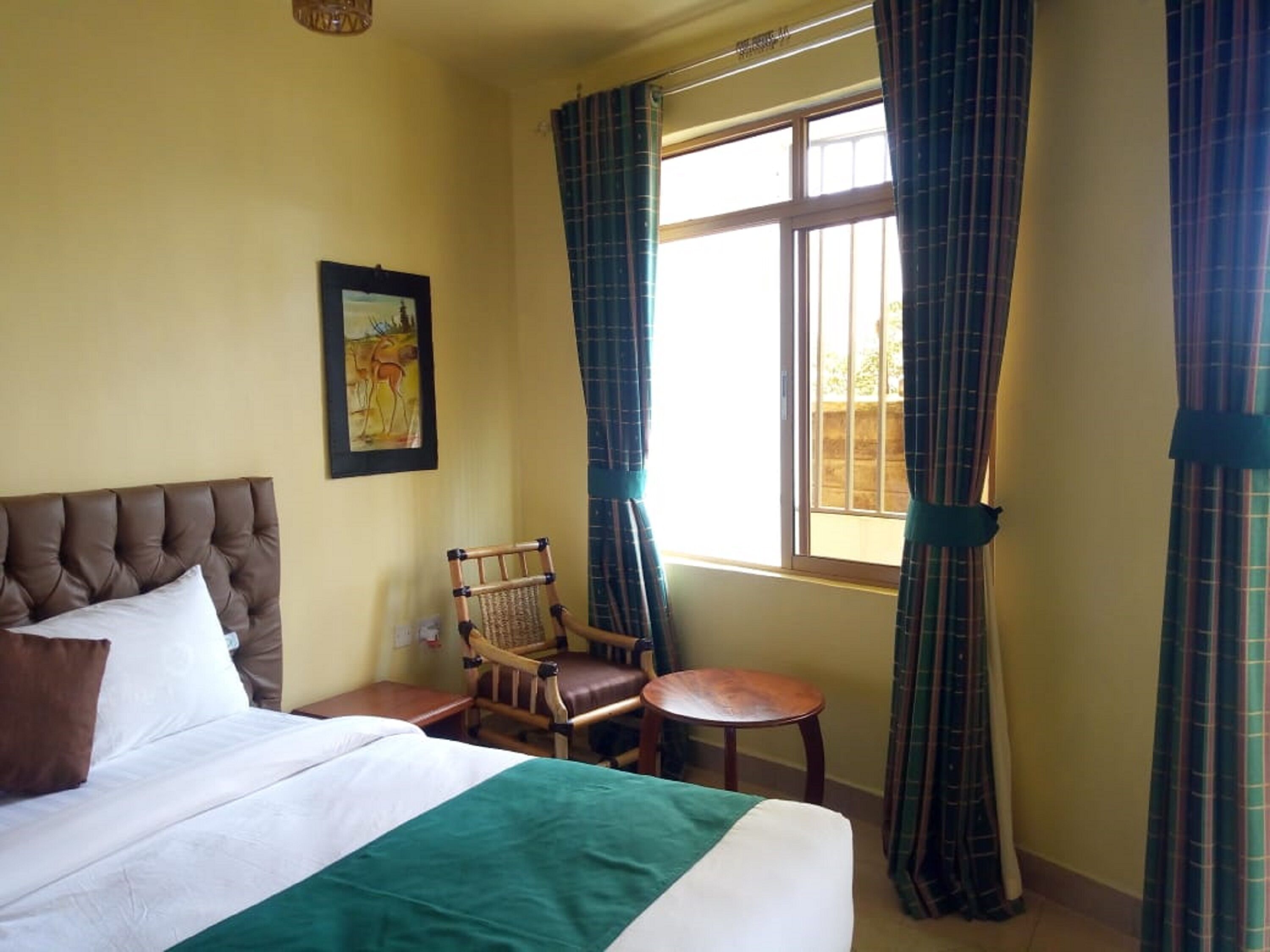 A hotel room with a bed, a chair, a small table, and a window with curtains.