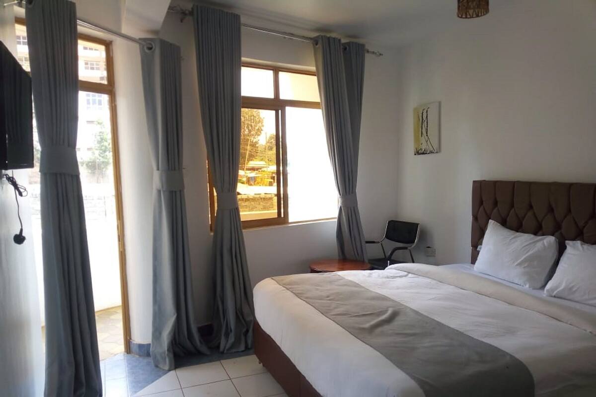A hotel room with a large bed, a chair, a TV, and a window with curtains.