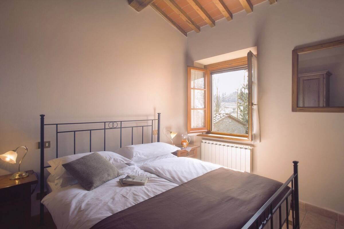 A bedroom with a bed, bedside lamps, a window, and a radiator.