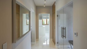 Corredor moderno com porta de vidro que dá para um banheiro, um espelho à esquerda e uma porta à direita.
