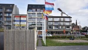A modern building with multiple balconies, a swing set, and a flagpole with flags. - Tasteful Apartment Near the Centre and Beach of Bredene (Bredene)