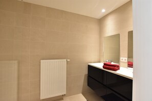 Une salle de bain moderne avec des carreaux de couleur beige, un radiateur blanc, un meuble-lavabo noir et une serviette rouge posée sur le comptoir.