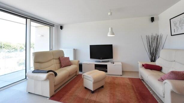 A modern living room with a sofa, ottoman, TV, and a large window. - Tasteful Apartment Near the Centre and Beach of Bredene (Bredene)