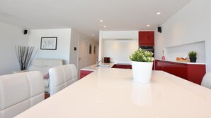 A modern living room with a white sofa, a dining table, and a kitchen area with red cabinets. - Tasteful Apartment Near the Centre and Beach of Bredene (Bredene)